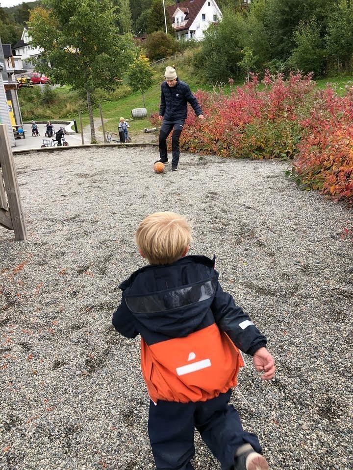 Halvor Egner Granerud sparker fotball med en liten gutt med lyst hår og regntøy.